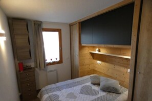 A bedroom with a bed, a dresser, a window with curtains, and built-in wooden shelves.