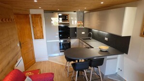 Une cuisine compacte dotée d’appareils électroménagers modernes, un coin repas avec une table et des chaises, et un canapé rouge agrémenté de coussins.