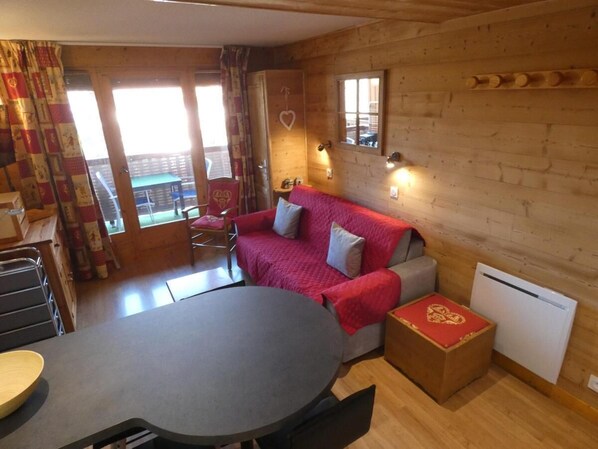 A cozy room with a wooden interior, a round table, a sofa with a red blanket, and a radiator.
