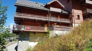 Un chalet en bois à plusieurs étages, doté de balcons et d’une fondation en pierre, sous un ciel dégagé.