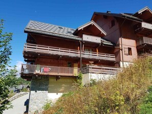 A multi-story wooden chalet with balconies, a stone foundation, and a clear sky. - 150m from ski slopes, Ground floor, balcony, tv, ski locker, 32m², Valloire (Valloire)