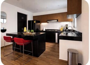 Cocina moderna con encimeras negras, armarios de madera, campana extractora de acero inoxidable y un cubo de basura pequeño.