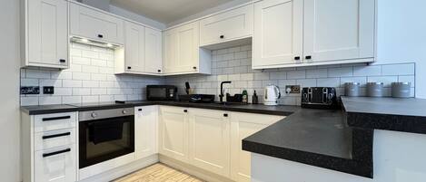 A modern kitchen with white cabinets, a black countertop, and a wooden floor.