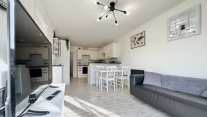 Una cocina moderna con armarios blancos, un comedor con sillas blancas y un sofá gris.