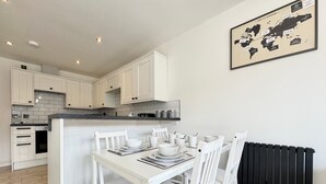 Una cocina moderna con armarios blancos, una mesa de comedor con platos y tazones blancos, y un radiador negro.