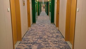 A hotel hallway with patterned carpet, wooden doors, and green walls. - Duoflai Hotel (Mudanjiang High-speed Railway Station No.4 Middle School) (Mudanjiang)