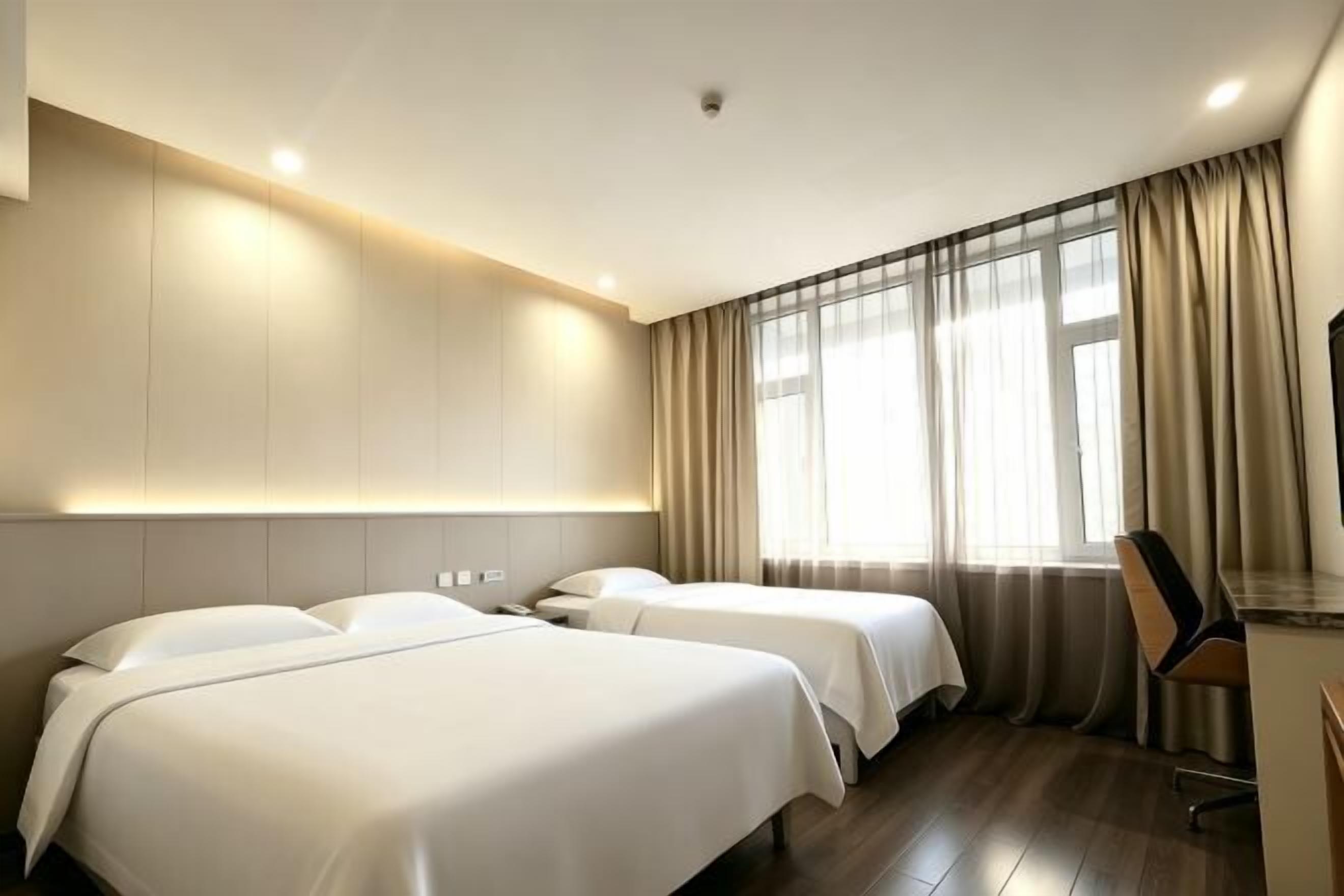 A hotel room with two beds, a desk, and a large window with curtains.