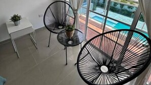 A balcony with two black wire chairs, a small table with a plant, and a view of a swimming pool.