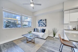 A modern living room with a white sofa, a coffee table, and a view of the city through large windows. - Trendy One Bedroom Getaway Steps from Biscayne (Miami)