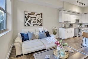 A modern living room with a sofa, a coffee table, and a kitchen area in the background. - Trendy One Bedroom Getaway Steps from Biscayne (Miami)