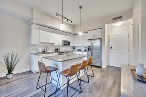 A modern kitchen with white cabinets, a stainless steel refrigerator, and a central island with bar stools. - Trendy One Bedroom Getaway Steps from Biscayne (Miami)