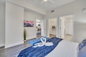 A modern bedroom with a large bed, a TV on the wall, and a view into the kitchen and bathroom. - Trendy One Bedroom Getaway Steps from Biscayne (Miami)