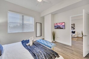 A modern bedroom with a large bed, a blue bench, a potted plant, and a view into another room. - Trendy One Bedroom Getaway Steps from Biscayne (Miami)
