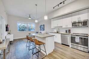 Una cocina moderna con armarios blancos, electrodomésticos de acero inoxidable, una barra con taburetes y un amplio ventanal con vistas al exterior.