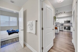 Un apartamento moderno con dormitorio, baño y cocina. El dormitorio tiene una cama con una manta azul y una toalla blanca colgada en la pared. El baño tiene una toalla blanca colgada en la pared. La cocina cuenta con electrodomésticos de acero inoxidable y una planta en la encimera.