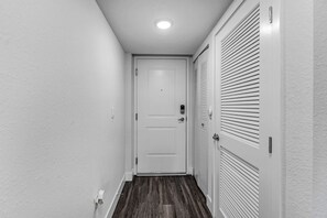 A narrow hallway with a white door at the end, a light switch on the wall, and a vent on the right. - Stylish 1BR Unit W/ Free Parking | Near Wynwood (Miami)