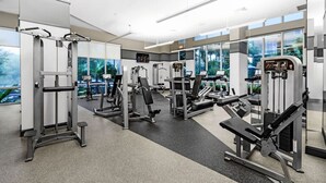 A modern gym with various exercise machines, large windows, and a view of greenery outside.