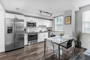 A modern kitchen with stainless steel appliances, white cabinetry, and a dining area with a table and chairs. - Stylish 1BR Unit W/ Free Parking | Near Wynwood (Miami)