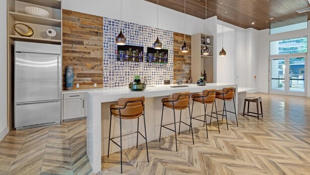A modern kitchen with a herringbone wood floor, a central island with bar stools, a built-in refrigerator, and pendant lighting.