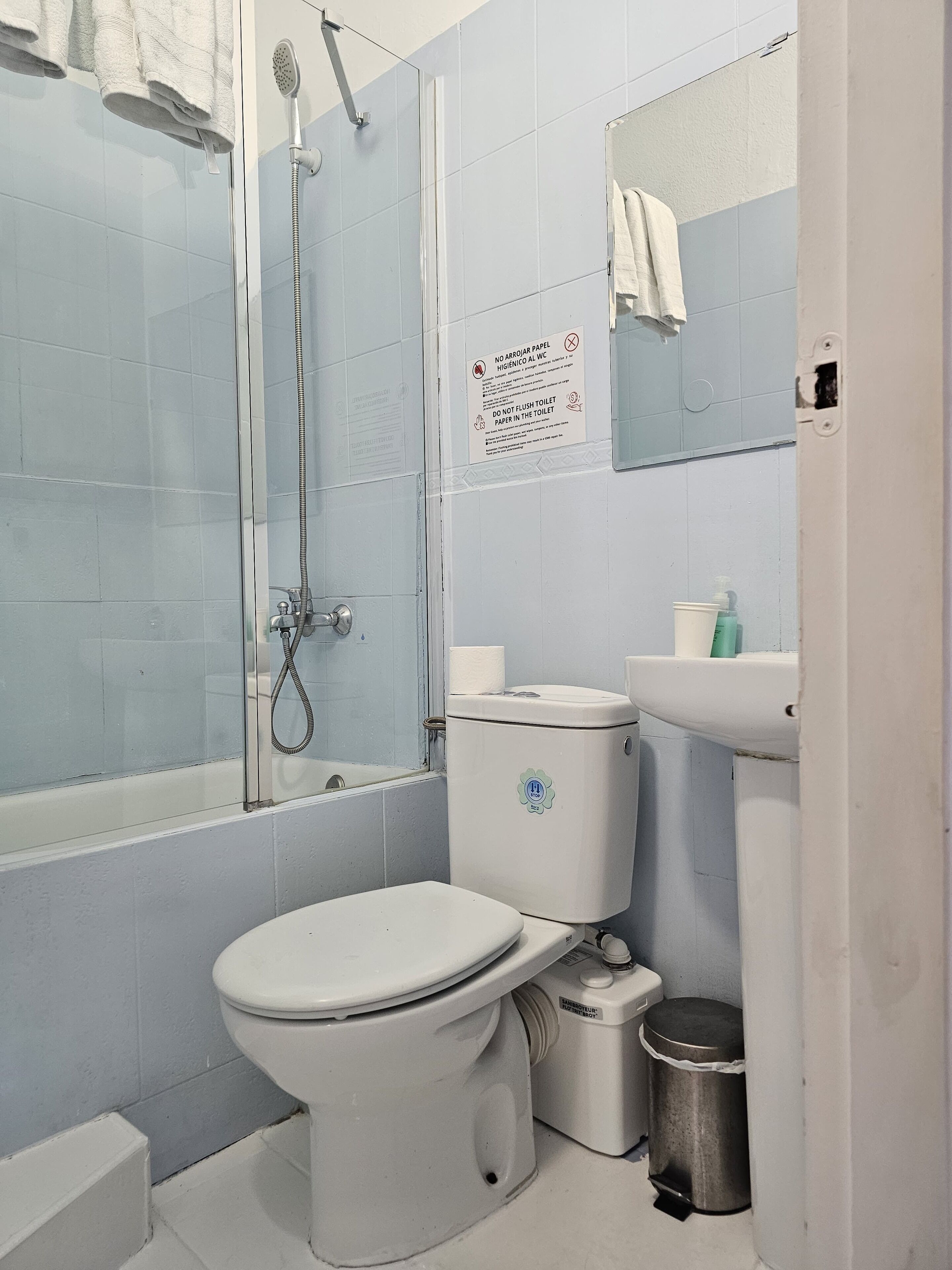 Een badkamer met toilet, wastafel en douche. Er hangt een bord met instructies aan de muur.