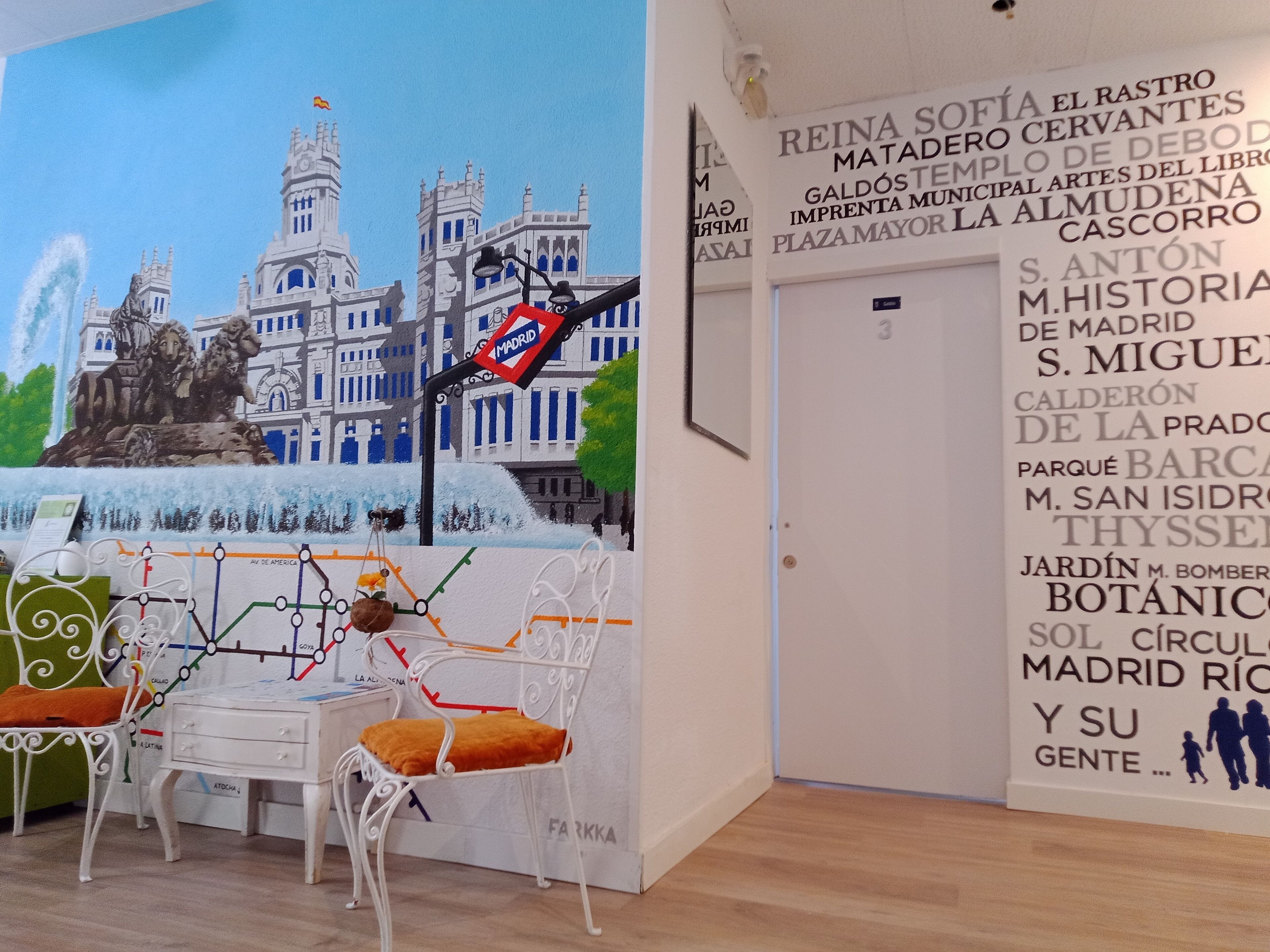 Une pièce ornée d’une fresque représentant un bâtiment historique, d’une carte et d’un coin salon avec une petite table et des chaises.