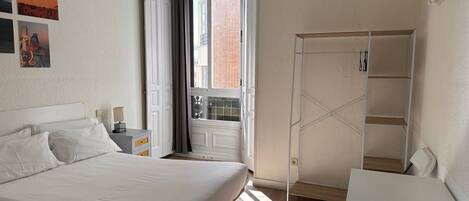 A bedroom with a bed, a bedside table, a wardrobe, and a window with curtains.