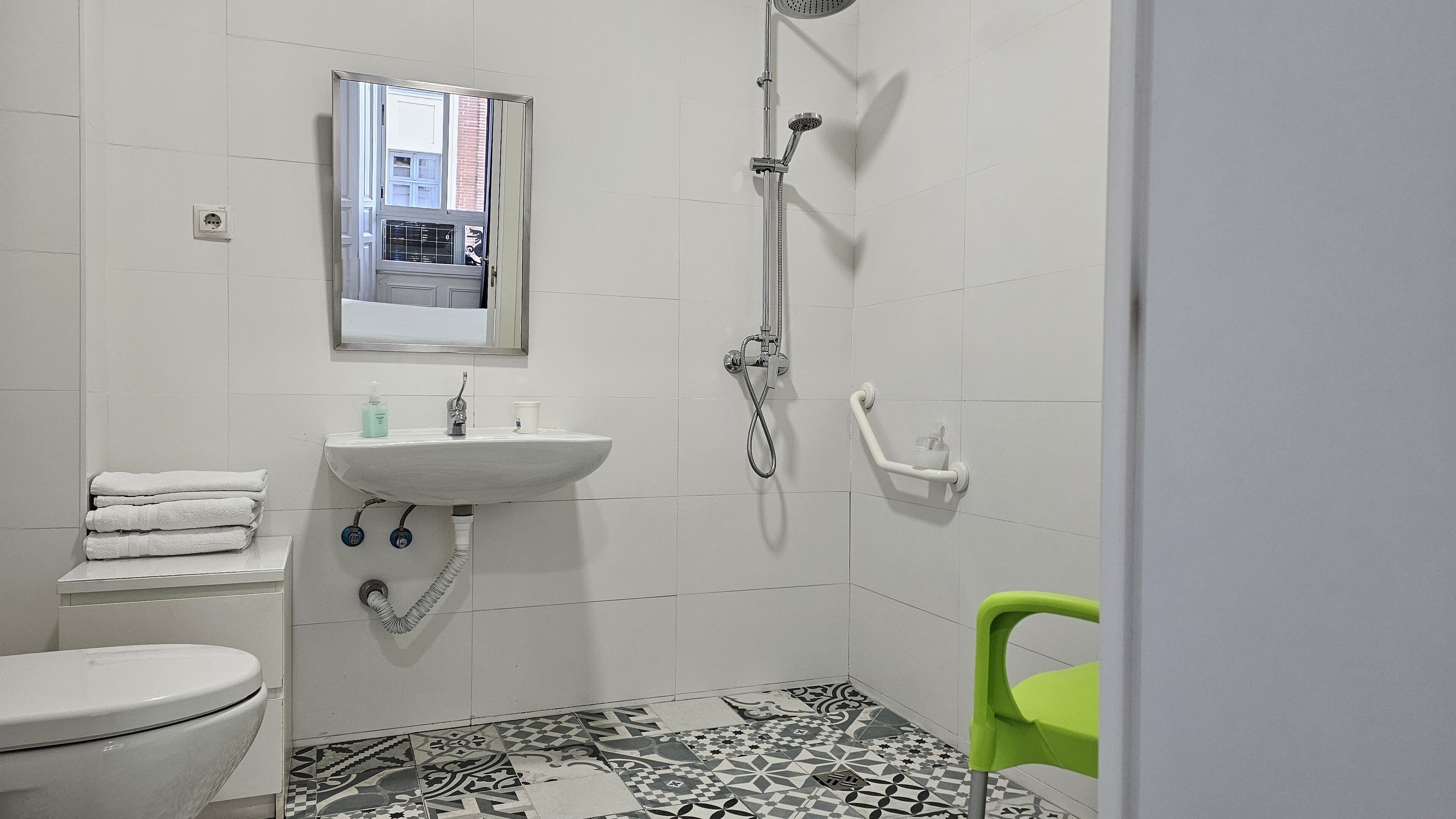Un baño con inodoro, lavamanos, ducha y una silla verde.