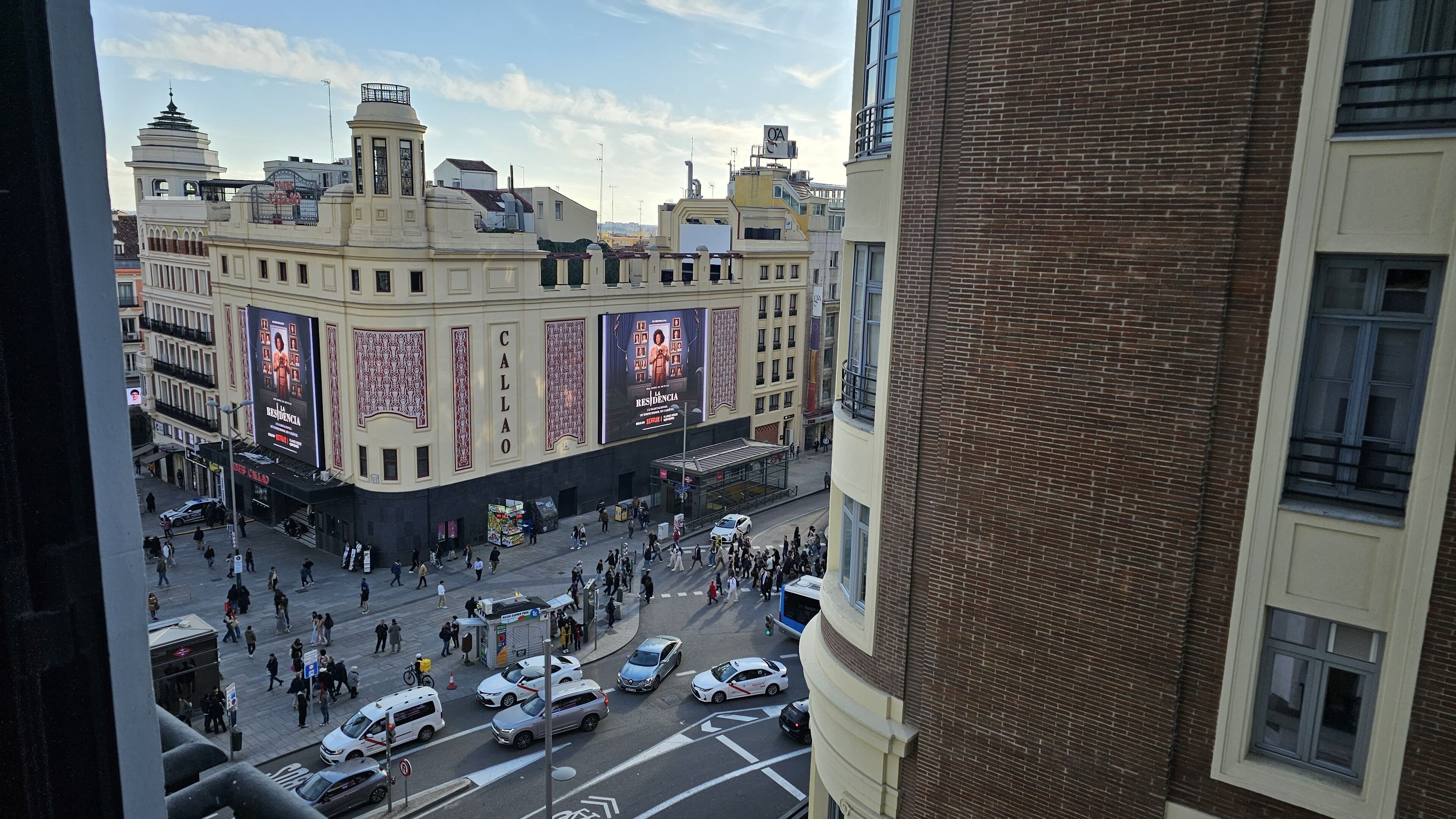 Una concurrida calle urbana con un edificio histórico que presenta grandes anuncios y una entrada destacada.