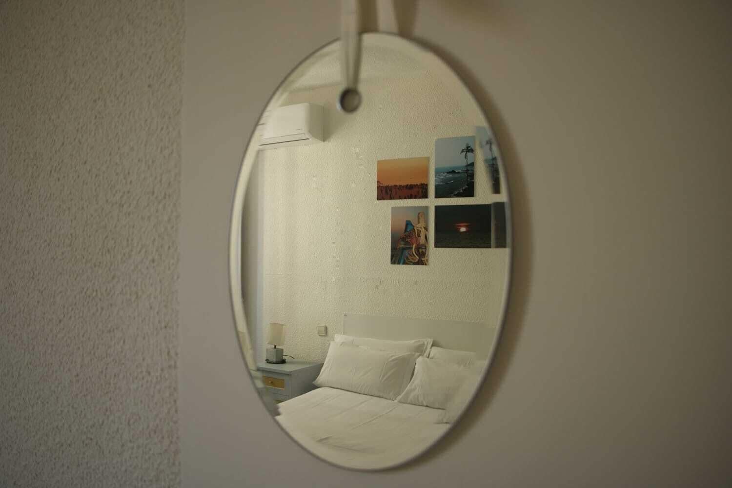 Ein runder Spiegel, der ein Bett, einen Nachttisch und eine Wand mit Bildern widerspiegelt.