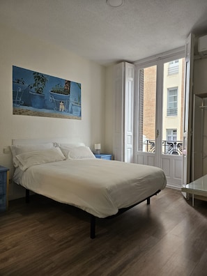 A bedroom with a bed, a nightstand, a lamp, a painting, and a view of the outside. - Éxito en Madrid (Madrid)
