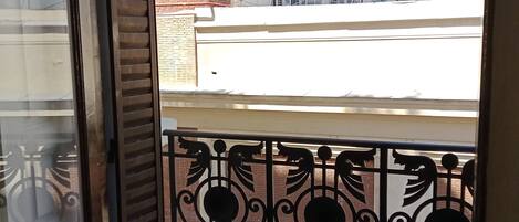 A balcony with a metal railing, a view of a brick building, and a white building in the background.