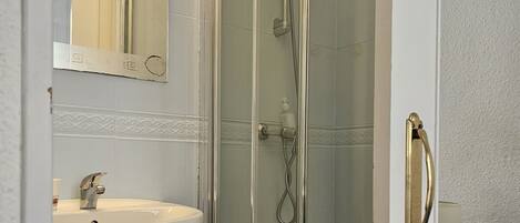 Un baño con ducha envuelta en vidrio, un lavamanos y un perchero para toallas.