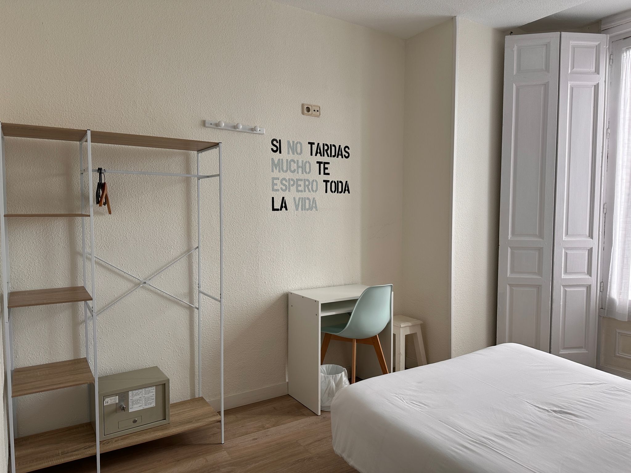 A bedroom with a bed, a desk, a chair, a wardrobe, and a wall-mounted shelf with a motivational quote.
