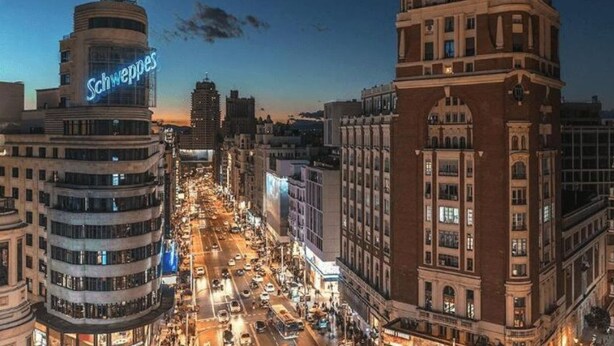 A cityscape at dusk with a prominent building labeled "Schweppes" and another with "EXITO EN MADRID" sign. - Éxito en Madrid (Madrid)