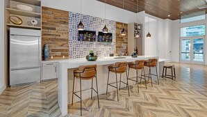 Une cuisine moderne avec un parquet en chevrons, un îlot central doté de tabourets, un réfrigérateur encastré et des luminaires suspendus.