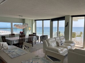 A spacious living area with a view of the beach, a dining table set with chairs, and a comfortable sofa.