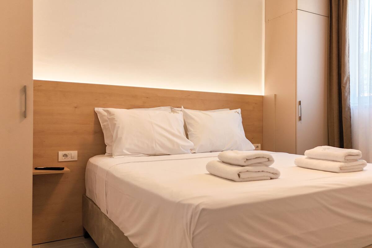 A neatly made bed with white linens and pillows, a wooden headboard, and a nightstand with a remote control.
