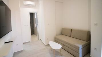 A modern living room with a beige sofa, a small white table, and a flat-screen TV mounted on the wall.