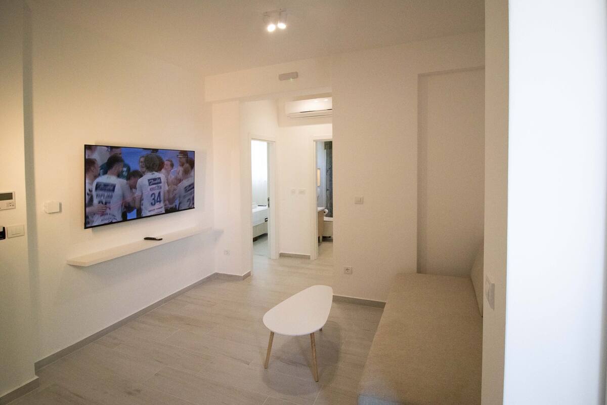 A modern living room with a flat-screen TV mounted on the wall, a white sofa, and a small white table.