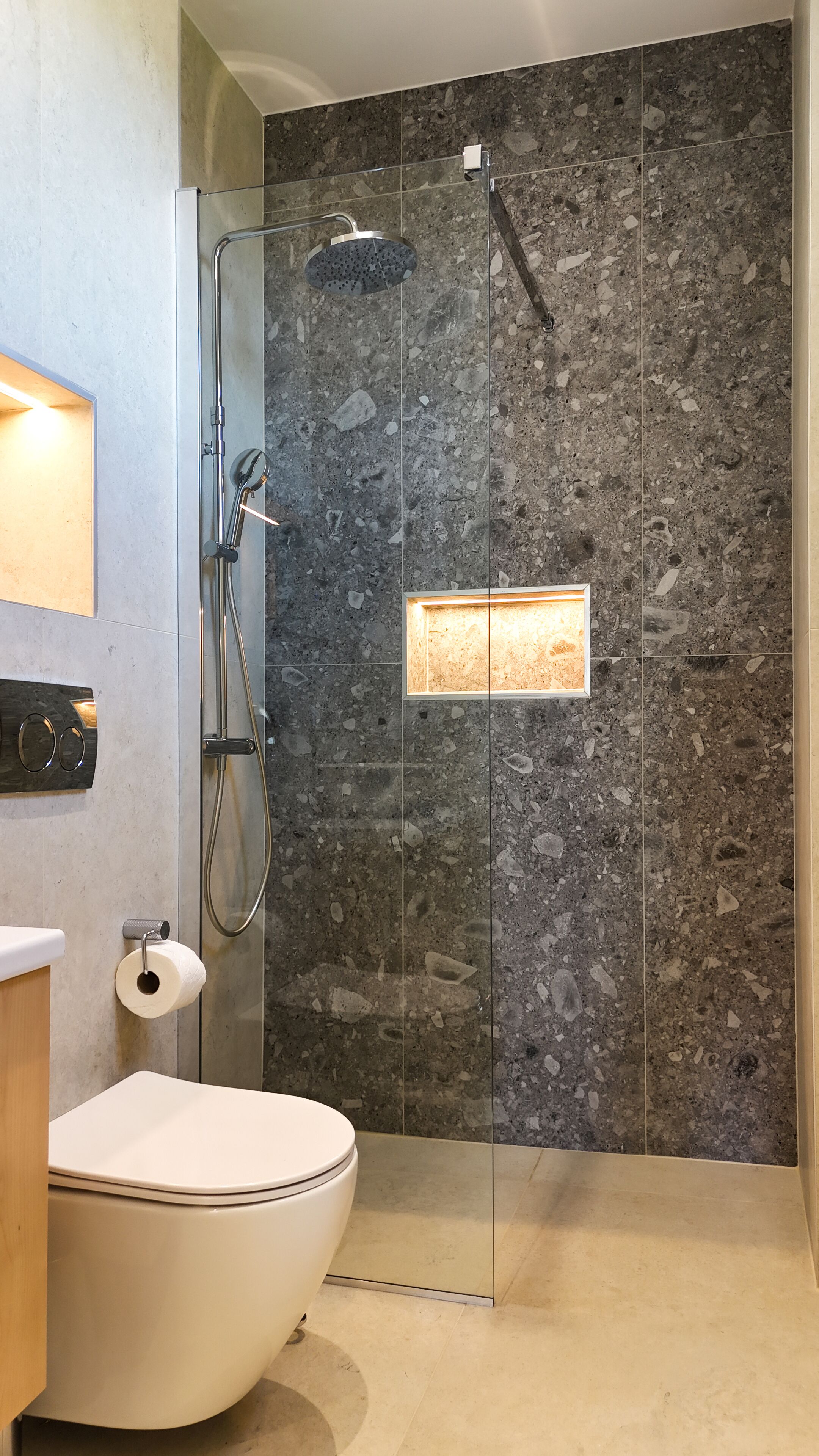 A modern bathroom with a glass-enclosed shower, a toilet, and a marble-tiled wall.