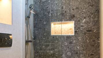 Une salle de bain moderne avec une douche à parois de verre, des toilettes et un mur recouvert de carreaux de marbre.