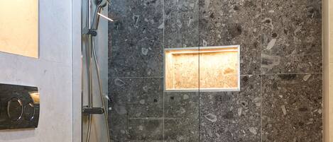 A modern bathroom with a glass-enclosed shower, a toilet, and a marble-tiled wall.