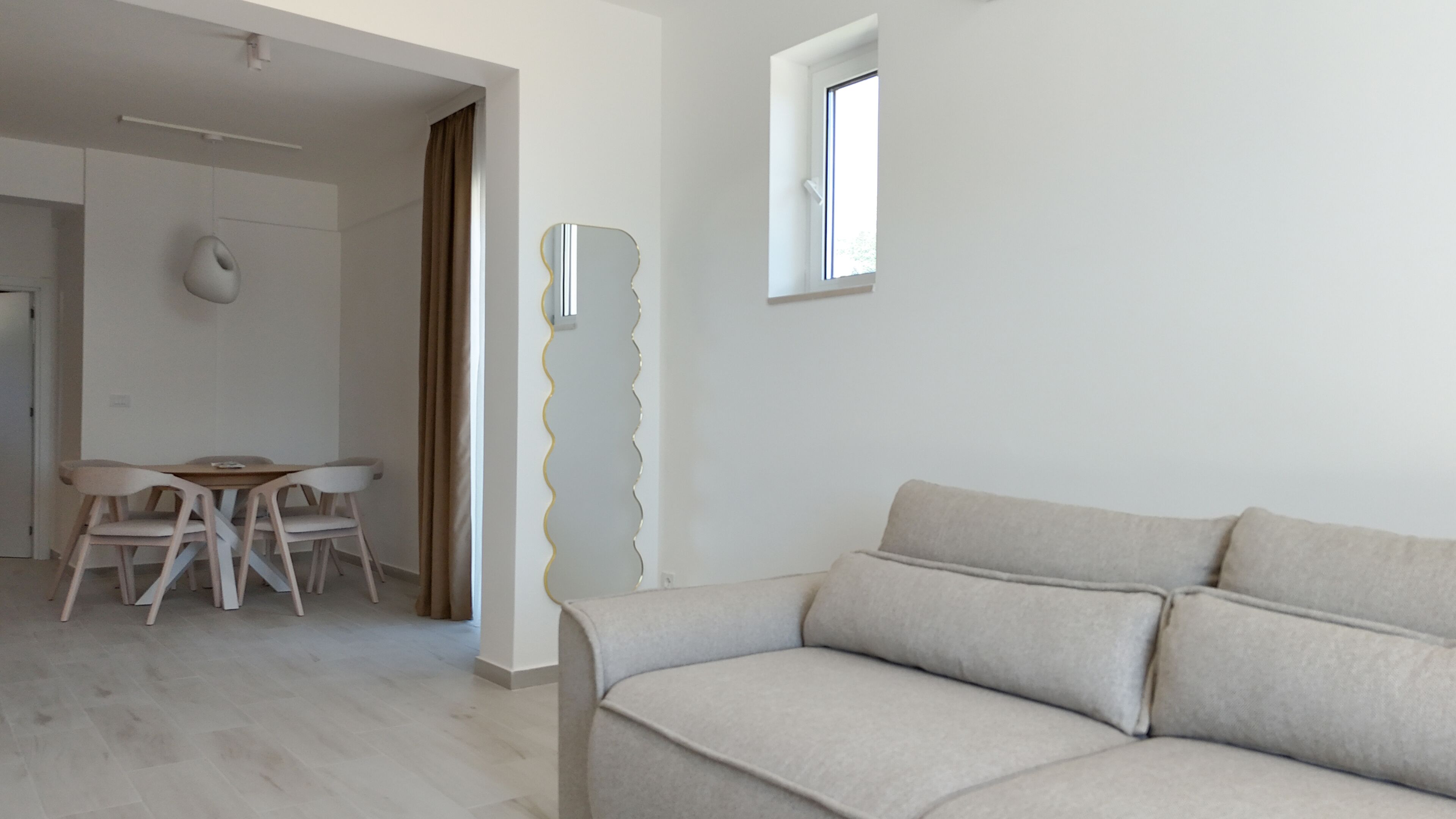 Una sala de estar moderna con un sofá, una mesa de comedor con sillas y un ventanal.