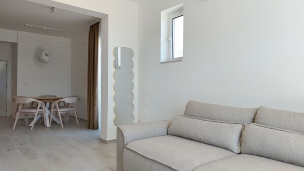 A modern living room with a sofa, a dining table with chairs, and a window. - Alpesa Apartments (Budva)