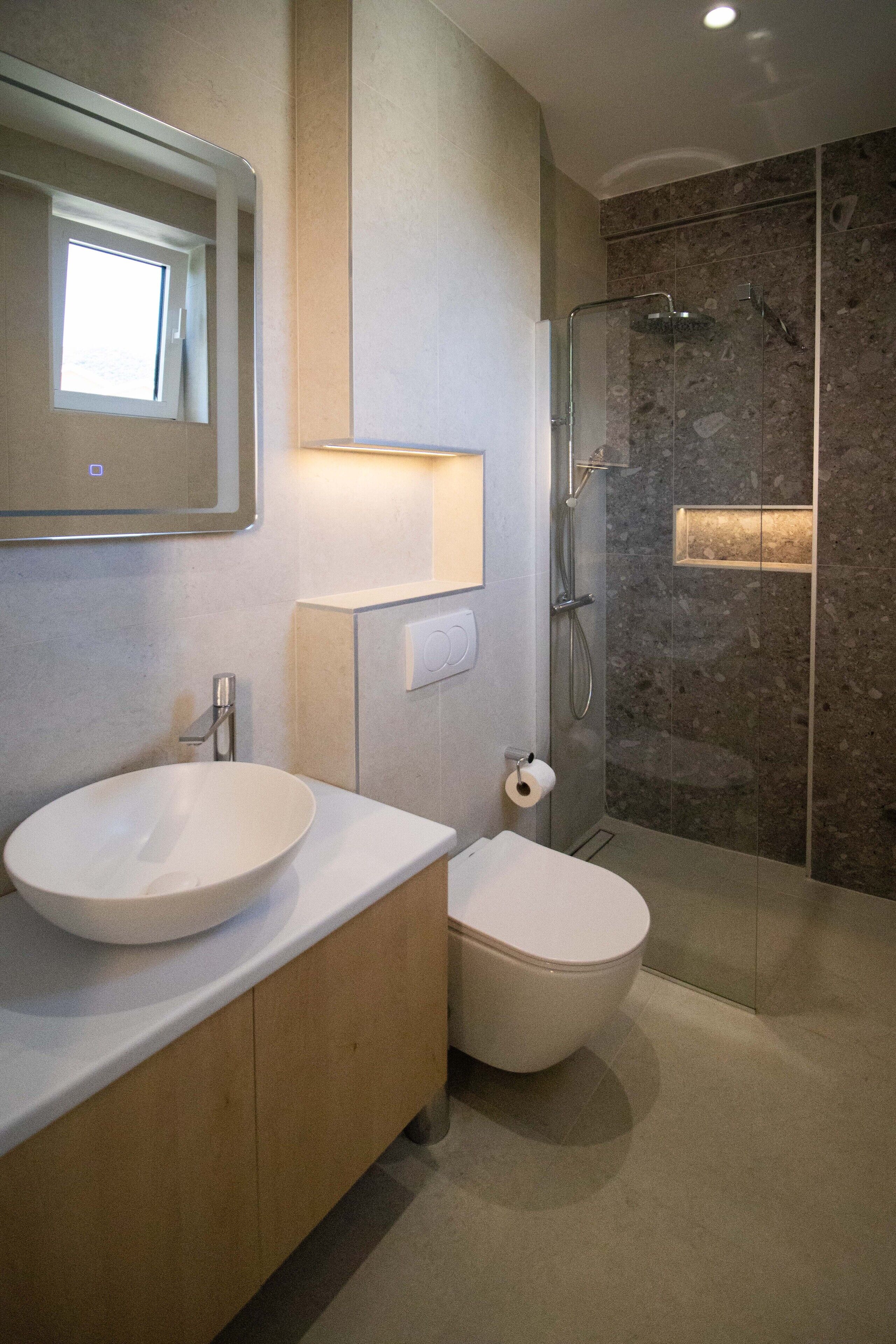 A modern bathroom with a large mirror, a round sink, a toilet, and a glass-enclosed shower.