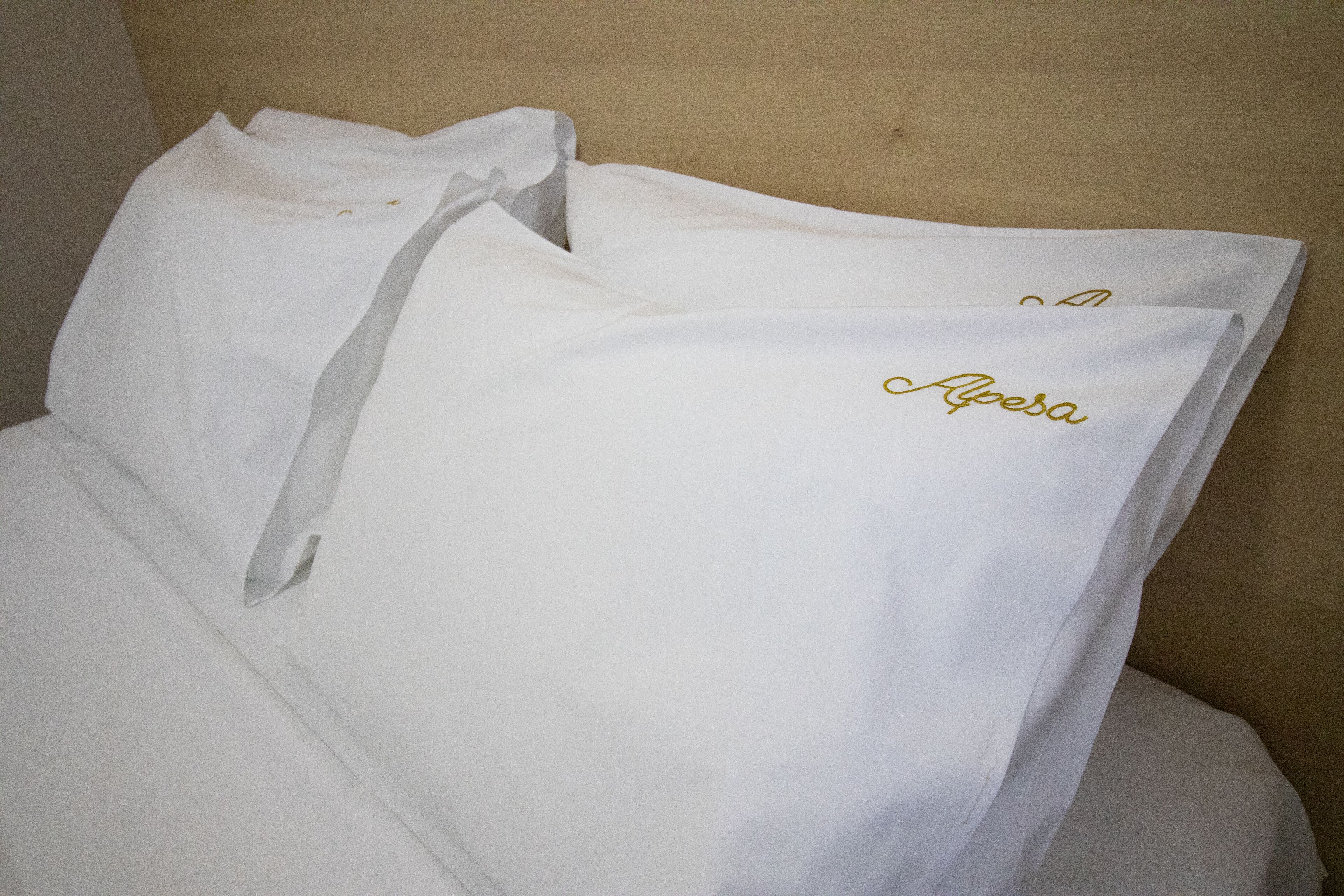 Una cama con ropa blanca y almohadas, una de ellas con el bordado 'Alpes'.