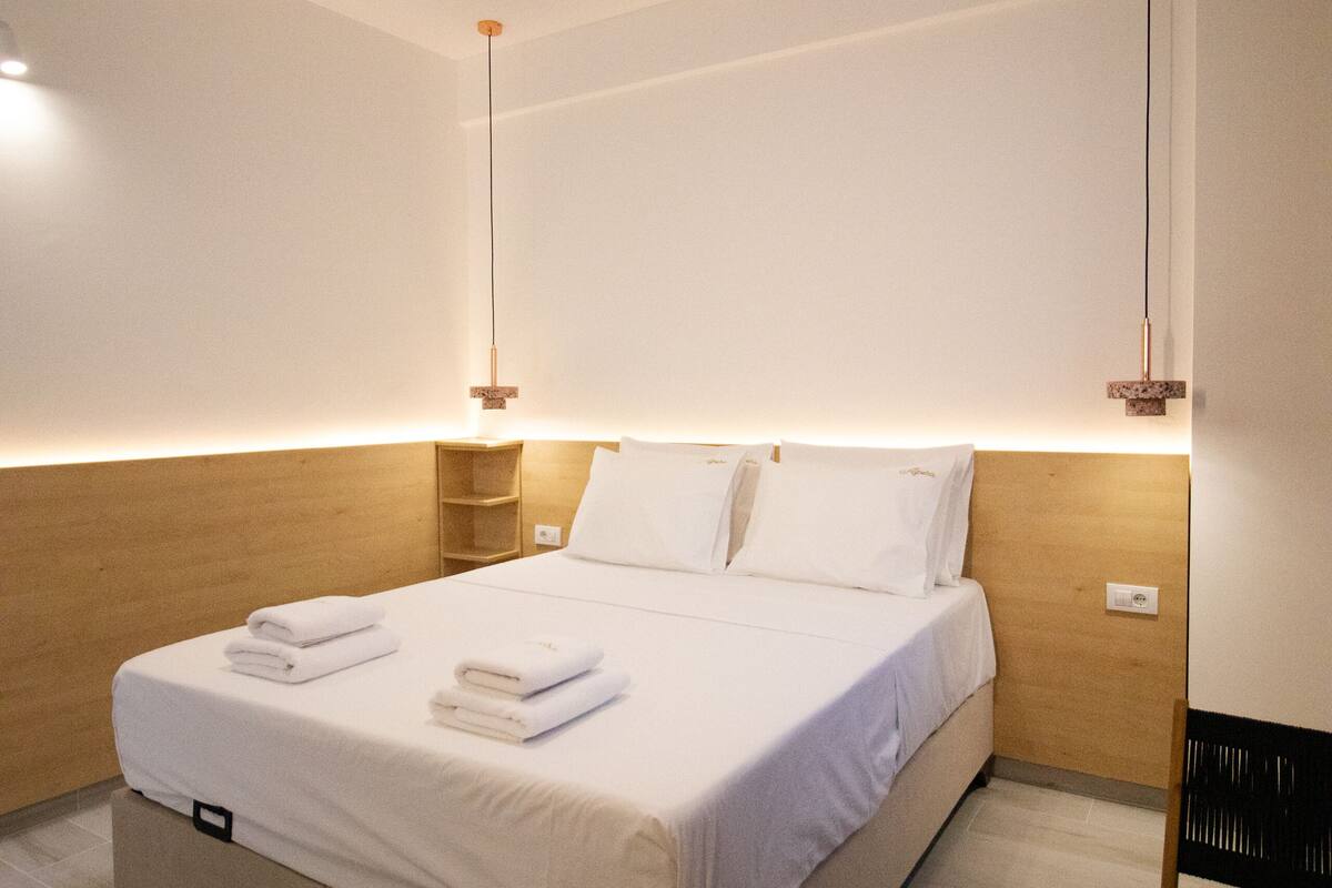 A modern hotel room with a large bed, wooden headboard, bedside tables, and a small wooden table.