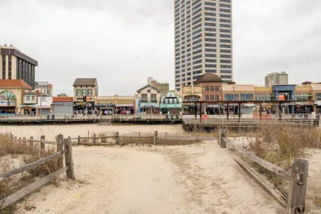 A coastal area with a sandy beach, wooden fence, and buildings including a tall hotel.