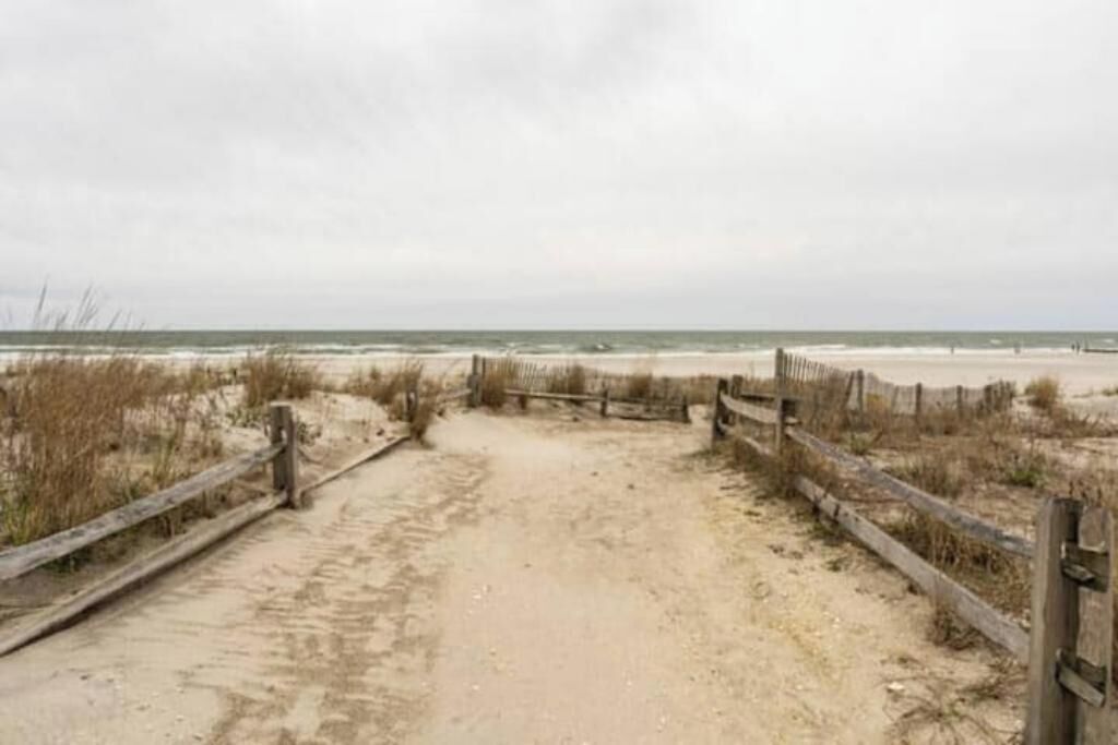 Ein sandiger Weg führt zu einem Strand, begleitet von einem Holzzaun auf beiden Seiten.