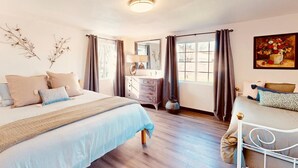 Un dormitorio con cama, mesita de noche, cómoda y una ventana con cortinas.